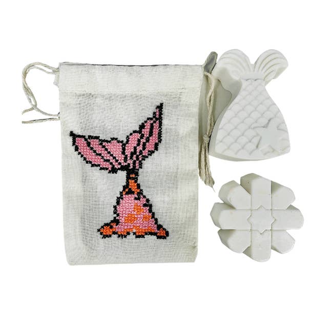 A soap pouch with an embroidered mermaid tail, a mermaid tail soap, and a shell shaped soap