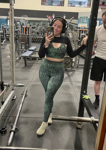 BuzzFeed writer is wearing the green snake skin patterned workout set with a black shrug and cream sneakers