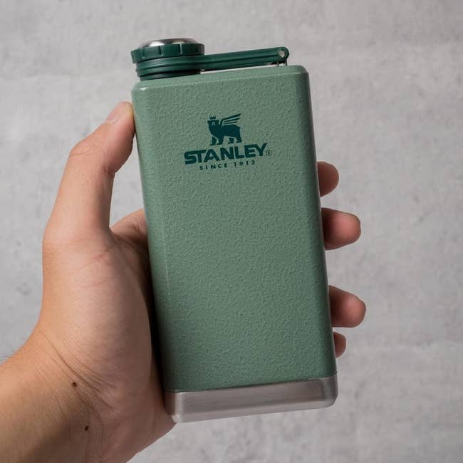 Hand holding a greenish Stanley flask with a metallic cap