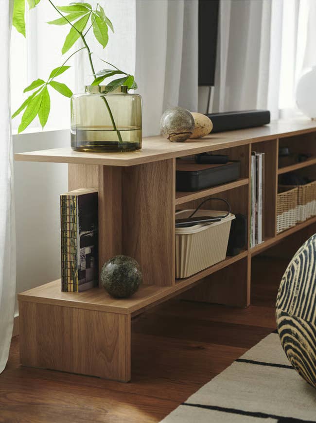 Wooden shelving unit with books, decorative stones, a vinyl player, and a green plant in a glass vase by a window, highlighting storage ideas