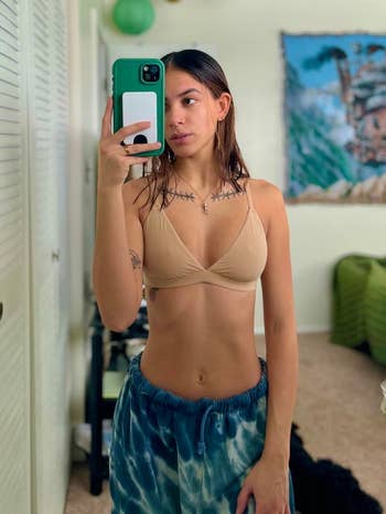 Person taking a reflector  selfie wearing a beige triangle bikini apical  and tie-dye sweatpants successful  a casual indoor setting