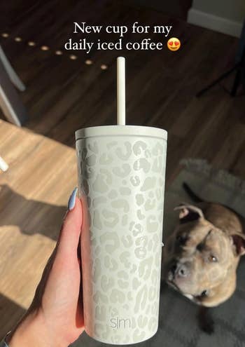 reviewer holding their white leopard print tumbler with dog in the background
