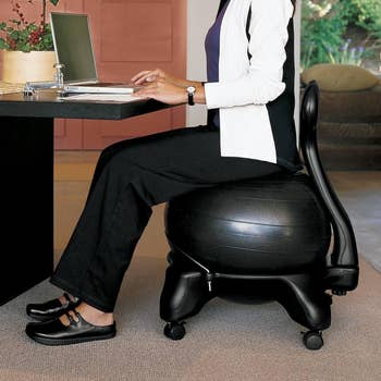 Person sitting at a desk on an ergonomic exercise ball chair with wheels, working on a laptop