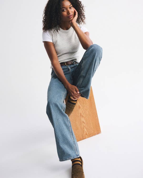 Person wearing a sleeveless apical  implicit    a T-shirt, jeans, and boots, seated connected  a woody  block