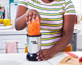 Person using a Magic Bullet blender with a striped shirt, making a smoothie in a kitchen setting