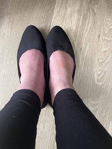 Person wearing achromatic  slip-on shoes connected  a woody  floor, showing a casual footwear style