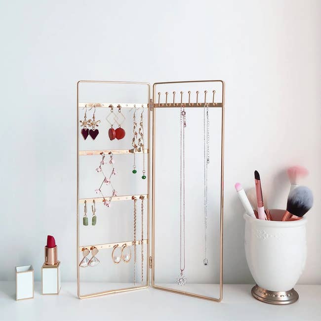 The gold bi-folding jewelry stand on a counter with baubles hanging off it