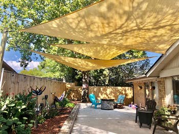 Backyard with 3  yellowish  triangle sunshades, seating area, plants, and decorative items, suggesting cozy outdoor surviving  abstraction  essentials for shopping