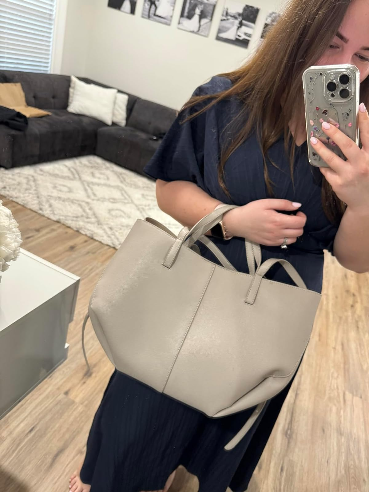 Reviewer in a dark dress holding a light gray tote bag, taking a selfie in a living room