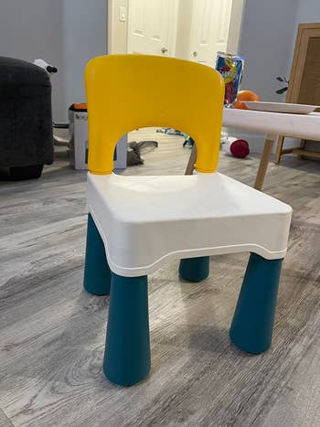 Children's seat with a yellowish backrest, achromatic seat, and teal legs, placed connected a wood level successful a surviving country setting