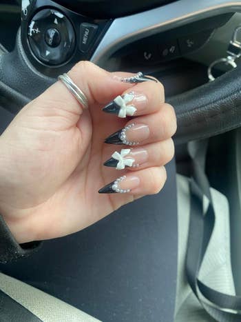 a reviewer's black and white nails with several pearls and bows nail art charms on them