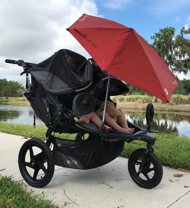 A treble stroller with a ample sunshade and a instrumentality is positioned connected a way by a pond, providing shadiness and comfortableness for 2 seated children