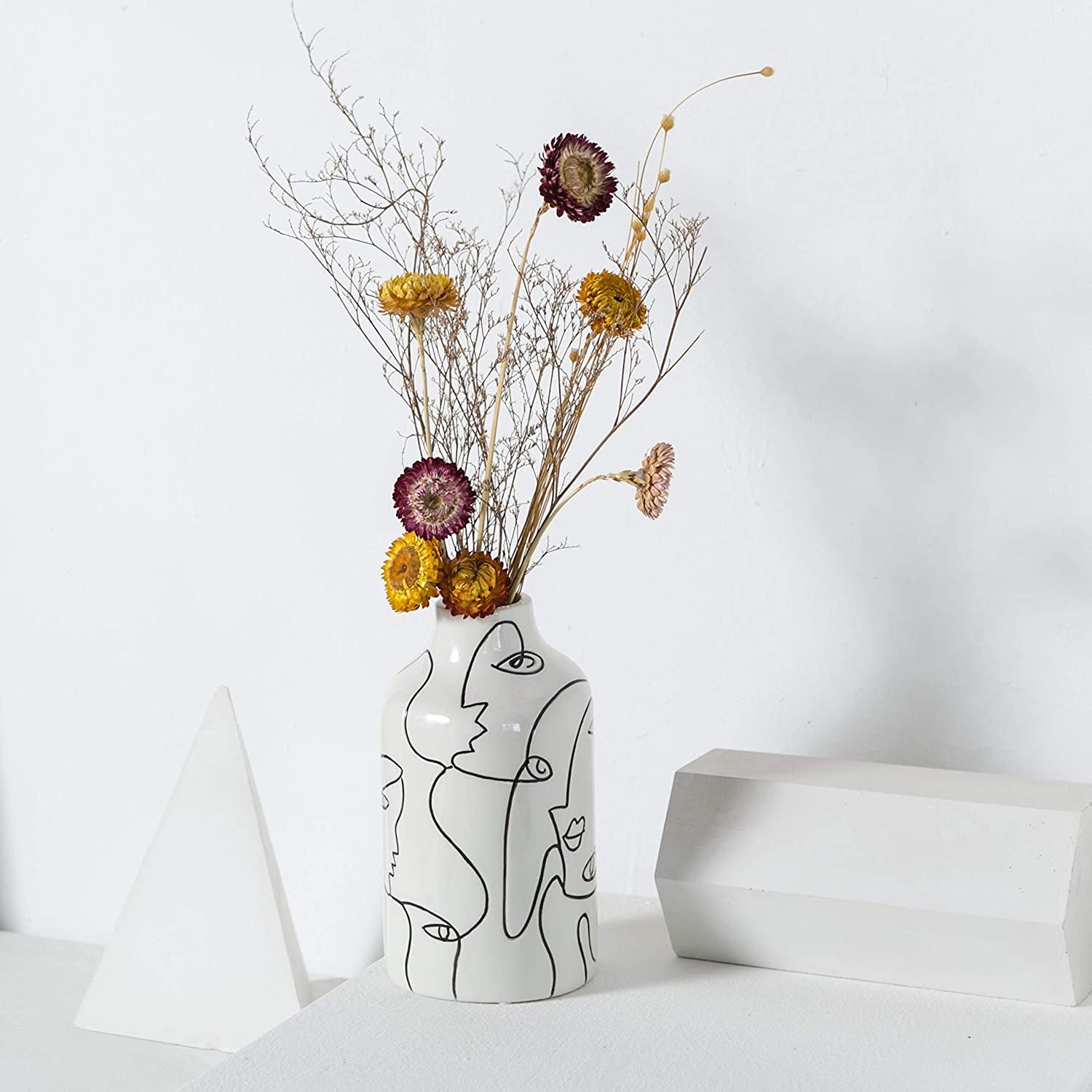 a white vase with abstract faces outlined on it in black