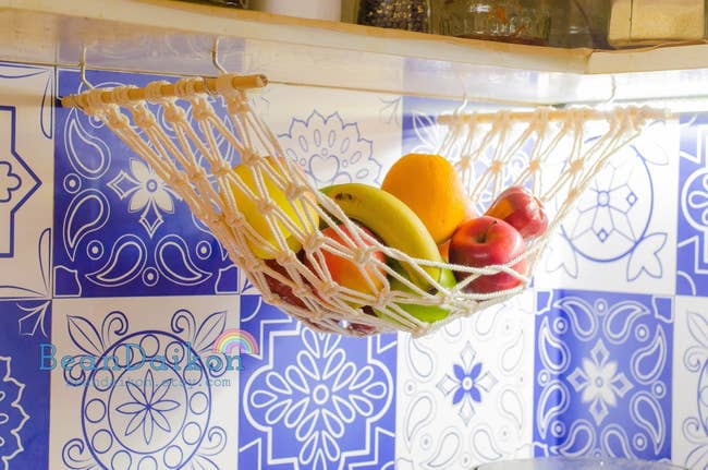 the macrame fruit hammock filled with fruit and mounted under a kitchen cabinet