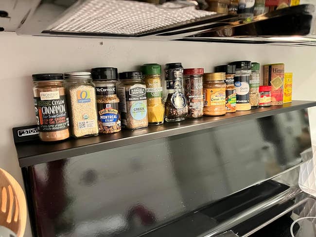 reviewer's black magnetic shelf on top of stove holding spices