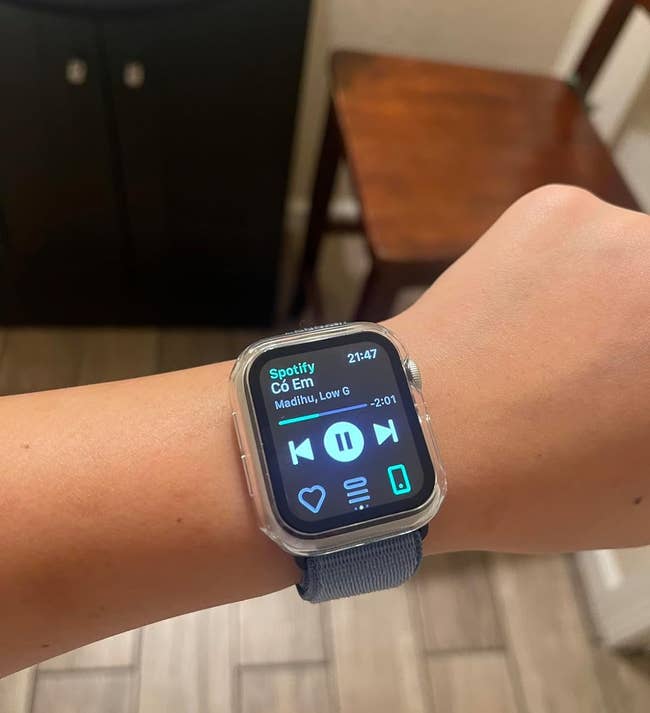 Person wearing Apple watch displaying Spotify music controls on screen