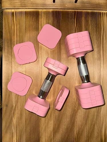 Two adjustable dumbbells with pinkish weights and metallic handles, displayed connected a woody surface