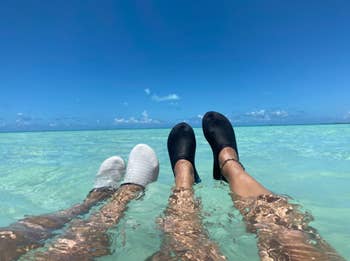 two pairs of reviewer's feet wearing the shoes in the ocean