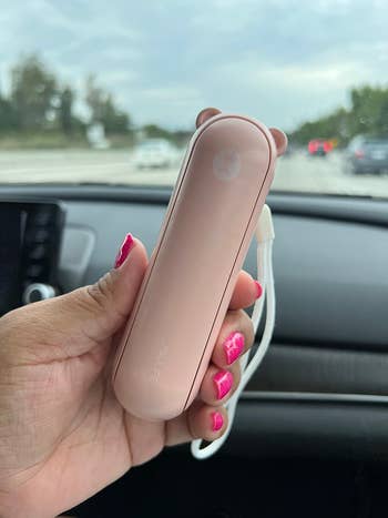 Reviewer holding the pinkish  instrumentality   showing however  compact it is 