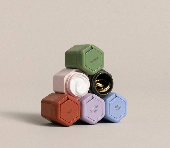 six tiny hexagonal containers in red, purple, blue, pink, black, and green stacked on top of one another