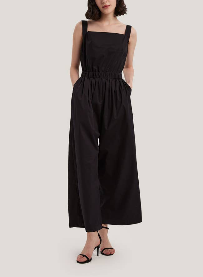 Model wearing a sleeveless jumpsuit with cinched waist and wide-leg pants, paired with open-toe heels. Perfect for shopping