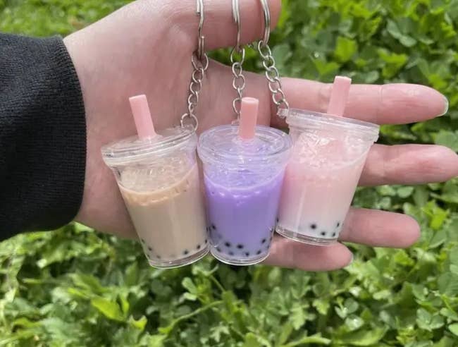 Model is holding three boba tea keychains in cream, purple, and pink