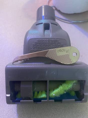 Vacuum attachment with spinning brush and a cleaning tool resting on top, used for maintaining clean bristles and optimal vacuum performance