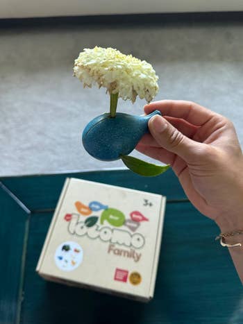 Hand holding a artifact  vase shaped similar  a whale with a flower, implicit    a container  labeled 