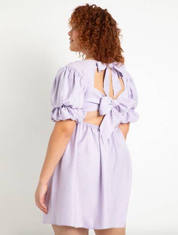 a model showing the back of a knee length lavender dress with two bows securing the open back