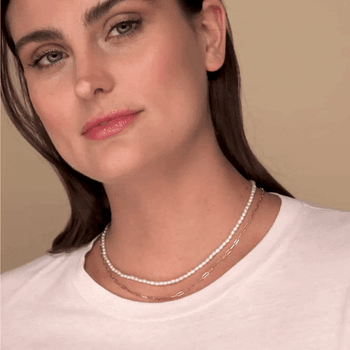 gif of a model wearing a small string of pearls layered with a dainty gold necklace