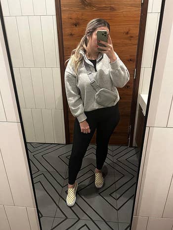 reviewer wearing the gray pullover with black leggings and checkered Vans sneakers