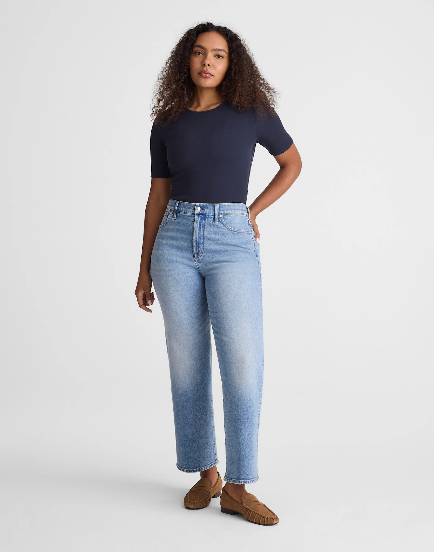 Person wearing a fitted short-sleeve shirt, high-waisted wide-leg jeans, and loafers, posing with one hand on hip