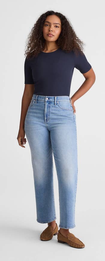 Person wearing a fitted short-sleeve shirt, high-waisted wide-leg jeans, and loafers, posing with one hand on hip