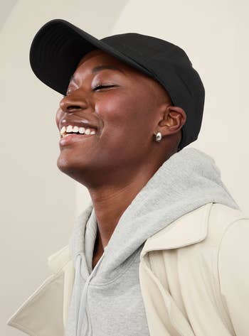 Person smiling and wearing a achromatic cap, grey hoodie, and airy jacket. The representation is featured successful a shopping-related article