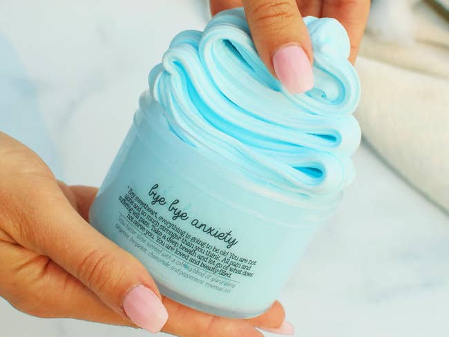 a model's hand holding a container of light blue therapy dough
