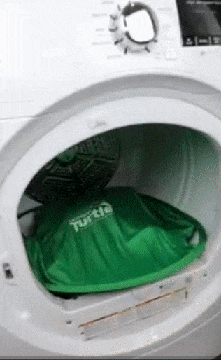 A person using a green net with flexible outer rods to place on top of clothes in the dryer and scoop them out 