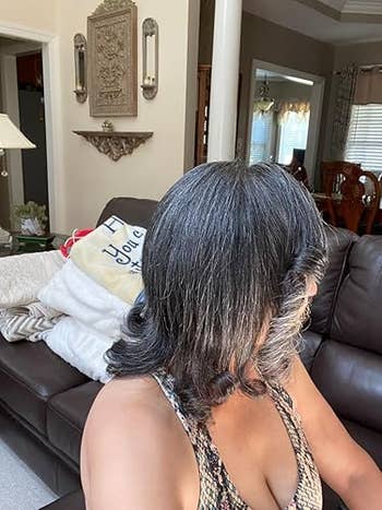 A pistillate with shoulder-length hairsbreadth sits connected a sofa successful a surviving room, looking away. She wears a patterned apical and a broad is seen down her