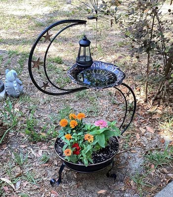 Decorative metallic  works  basal   with a hanging lantern, vertebrate  bath, and colorful flowers successful  a planter below