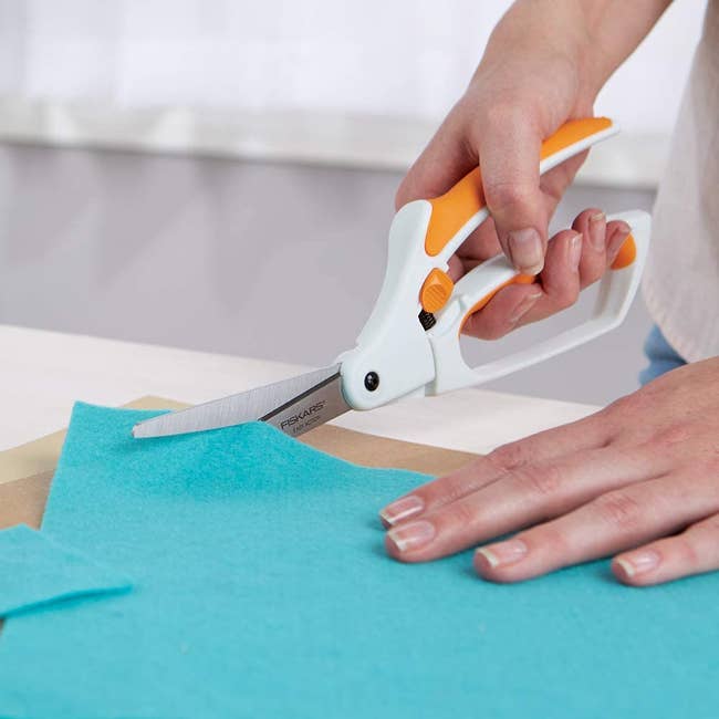 Model using white scissors with grip bottom and spring action top to cut a piece of fabric 
