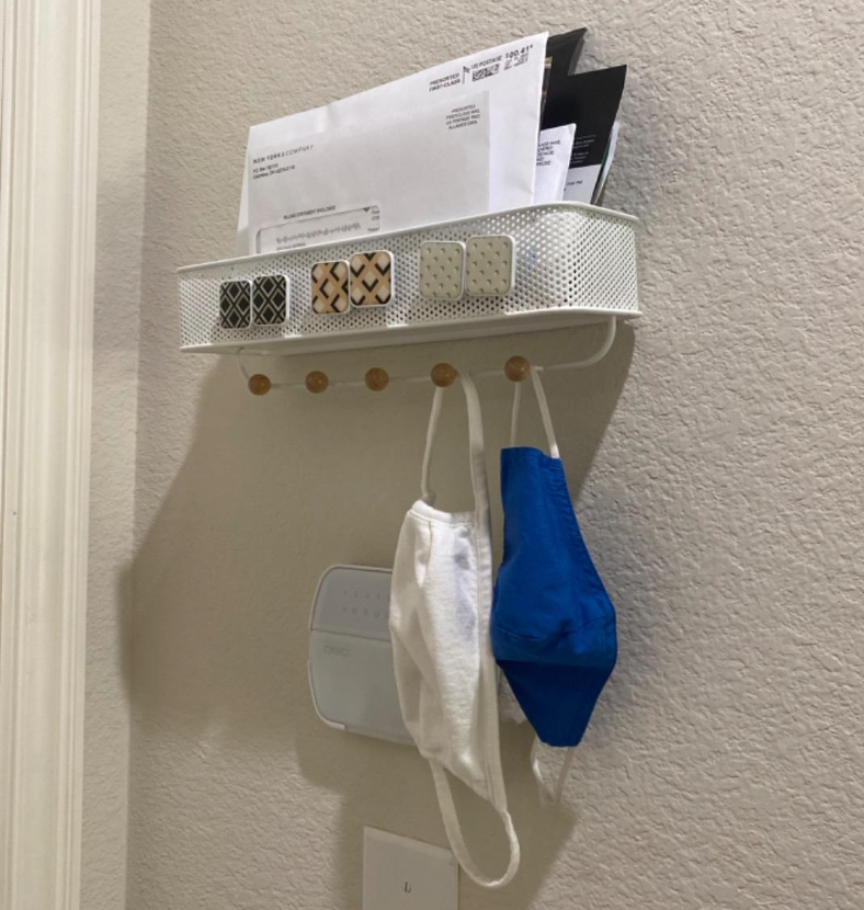 Reviewer pic of the white organizer with face masks hanging off the hooks and mail on the shelf on top