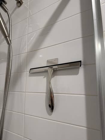 Shower squeegee hanging on a tiled wall next to a metal showerhead
