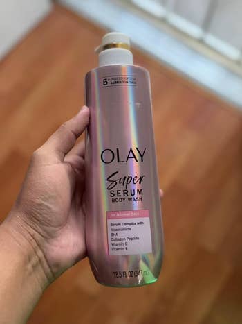 reviewer holding a vessel  of Olay Super Serum Body Wash for mean   skin, featuring serum analyzable  with niacinamide, BHA, collagen peptide, and vitamins