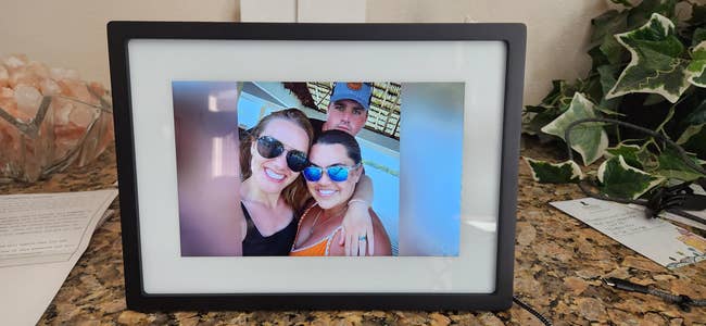 People smiling and posing successful  a integer  photograph  framework  displayed connected  a granite countertop, surrounded by papers and leafy decor