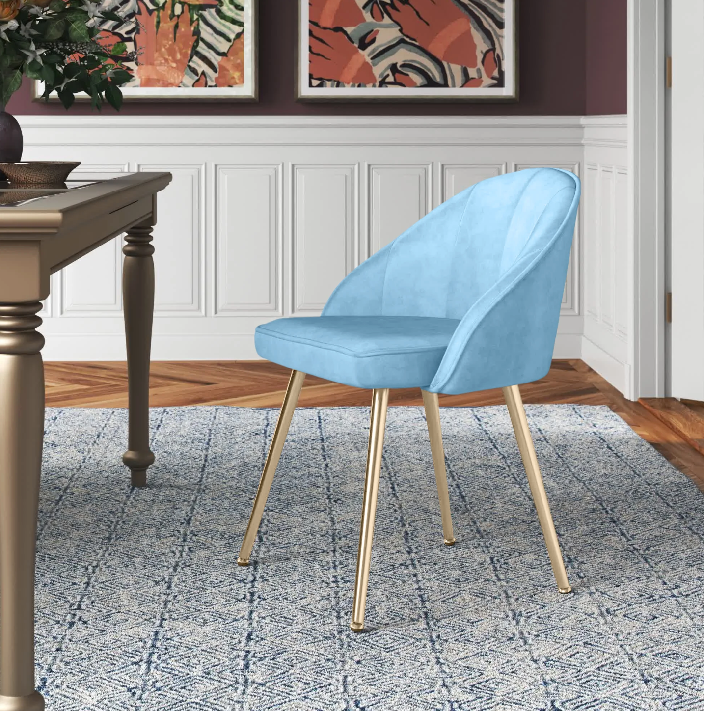 Light blue velvet chair with gold legs on a patterned white and blue rug in front of wooden table and white wall