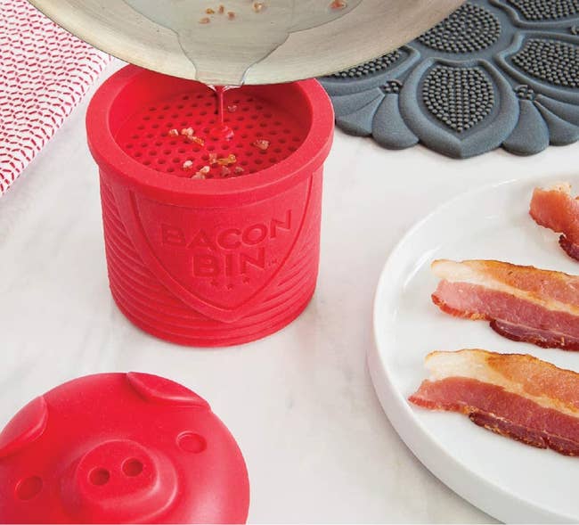 grease being poured into the red bacon bin on a counter next to a plate of bacon