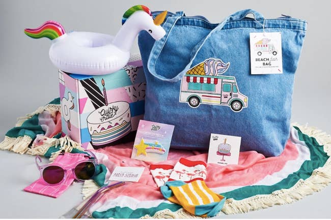 summer themed crate with unicorn drink float, sunglasses, denim tote, patches, metal straws, flamingo socks, and a beach blanket