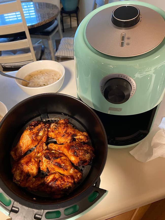 a reviewer using the blue air fryer to cook chicken wings. Showing an analog timer, round temperature dial, and convenient handle for removing the basket