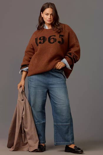 Person successful  casual attire poses holding a plaid blazer; wearing a sweater with 