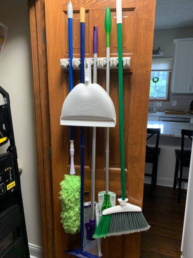 reviewer photo of the organizer neatly holding brooms and mops behind a closet door
