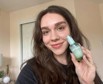 BuzzFeed writer holding the blue and green bottle of serum to their face